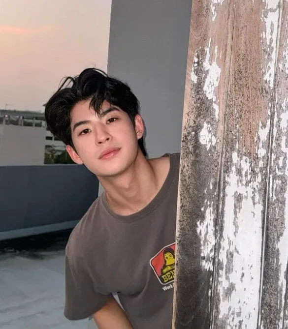 Mark Pakin Kunaanuwit mặc áo phông nâu chụp ngoài trời lúc chiều tà