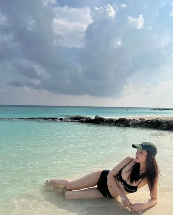 Ảnh JingJing Yu ngồi dưới làn nước biển trong xanh, đội mũ lưỡi trai