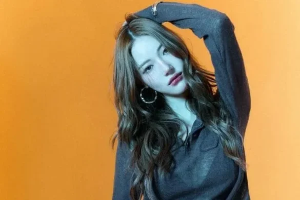 Ảnh JingJing Yu vắt tay lên đầu trên phông cam, áo len xám oversize